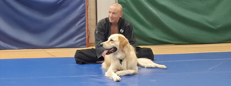 Yossi Sheriff and his dog, smiling on the blue mattress The Ninjutsu instructor is sitting on a blue mattress, stretching before training. A big golden retriever dog is sitting in front of him, both are smiling