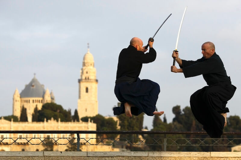 Two martial artists doing Ninjutsu practicing sword techniques in front of Jerusalem old city skyline